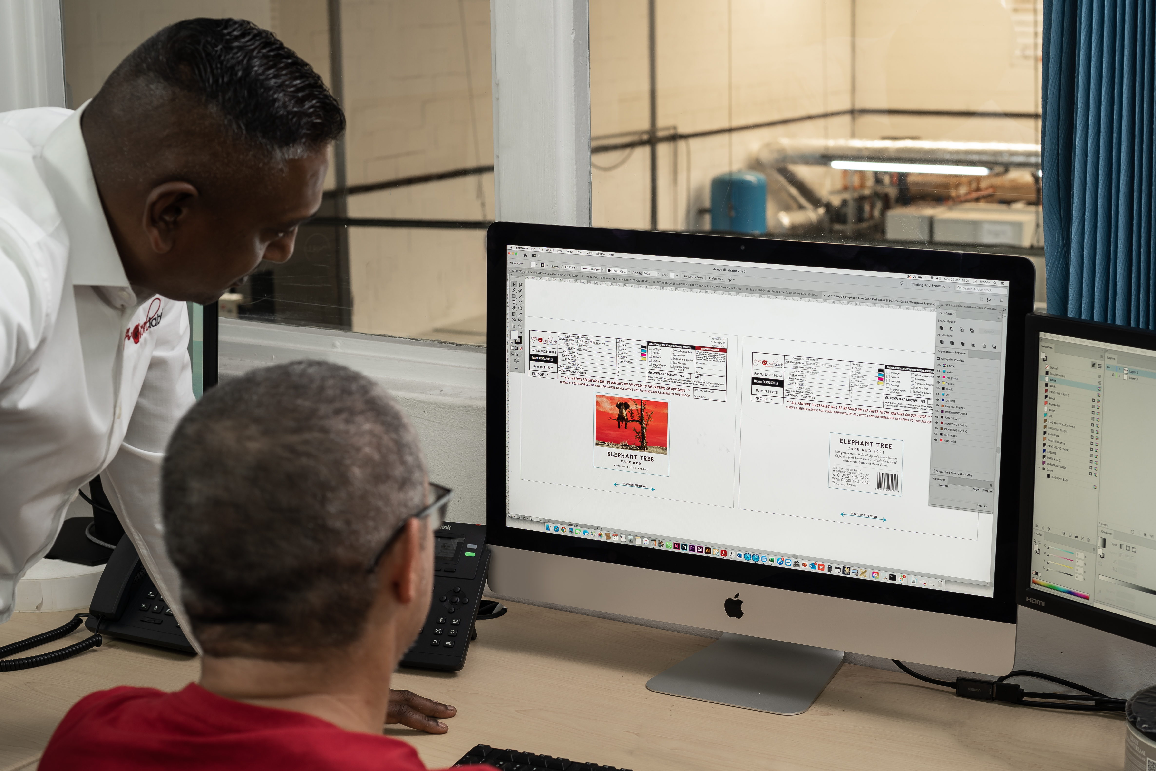 Two staff reviewing Elephant Tree wine label artwork in Adobe Illustrator on iMac